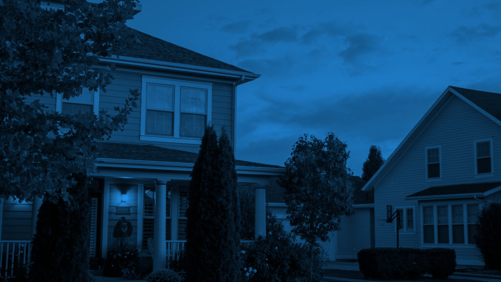 Two-story suburban house at dusk, porch light glowing beneath white columns and a wreath on the door